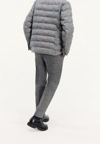 Graue Pufferjacke mit horizontalen Nähten, kombiniert mit passenden strukturierten Hosen und schwarzen Schuhen mit robusten Sohlen. Rote Akzente an der Jacke.