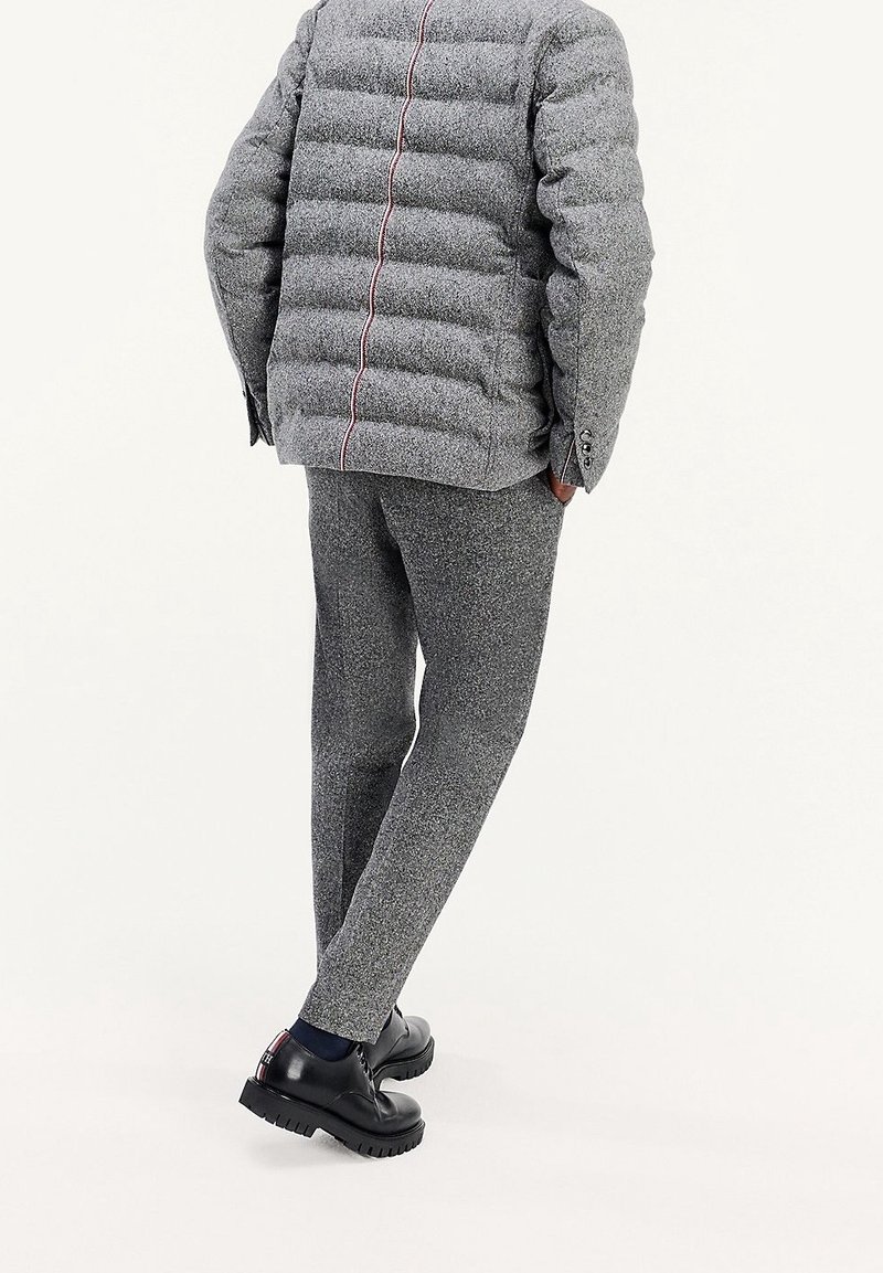 Graue Pufferjacke mit horizontalen Nähten, kombiniert mit passenden strukturierten Hosen und schwarzen Schuhen mit robusten Sohlen. Rote Akzente an der Jacke.