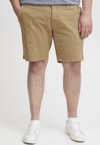 Khaki-Shorts aus Baumwollstoff, mit geradem Schnitt, Seitentaschen und angenähtem Saum. Kombiniert mit weißen Sneakers.