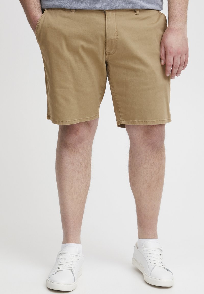 Khaki-Shorts aus Baumwollstoff, mit geradem Schnitt, Seitentaschen und angenähtem Saum. Kombiniert mit weißen Sneakers.