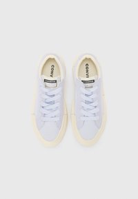 Light blue canvas sneakers with cream rubber soles, rounded toe, and traditional lace-up design. "Converse All Star" logo visible inside.