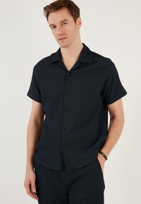 Korte mouwen, knoopshirt in donker marineblauw, met ribbelstructuur, een kraag en een ontspannen pasvorm. Zwarte knopen accentueren de voorkant.