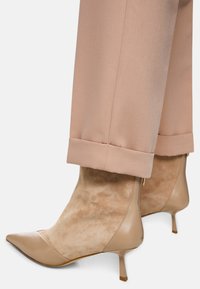 Beige spitze Stiefeletten mit glatt genarbtem Lederobermaterial, Wildlederakzenten und einem dünnen Kitten-Heel. Kombiniert mit hellrosa maßgeschneiderten Hosen.
