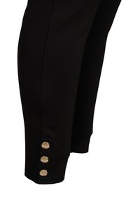 Musta leggings pehmest materjalist, mis on kujundatud sobivalt ja mille sääreosas on kolm tekstuurset kullatooni nuppu.