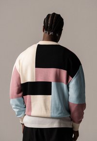 Maglione lavorato a maglia con un design in patchwork geometrico nei colori nero, crema, rosa e azzurro chiaro, con polsini e scollatura a coste per una maggiore texture.