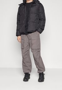 Černá péřová bunda s kapucí, šedé cargo kalhoty s velkými kapsami a černá obuv s texturovanými detaily. Pohodlný venkovní outfit.