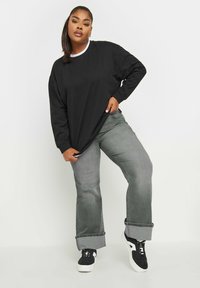 Camisa negra de manga larga con cuello blanco, combinada con unos vaqueros grises de pierna ancha, doblados en los puños, y zapatillas negras con suelas blancas.
