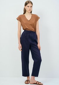 Brun bomull V-ringad T-shirt med uppvikta ärmar, i kombination med marinblå linnebyxor med dragsko i midjan och en avslappnad passform. Ljusbruna sandaler.