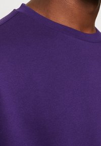 Felpa girocollo in cotone viola con un tessuto texture, caratterizzata da un colletto a coste e un aspetto liscio e uniforme.