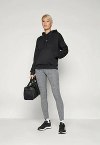 Juodas gobtuvu dėvimasis švarkas, pilkos sportinės kelnės ir juodi sportiniai bateliai. Modelis laiko juodą sportinę kuprinę. Lygus medvilnės audinys, laisvas fasonas.