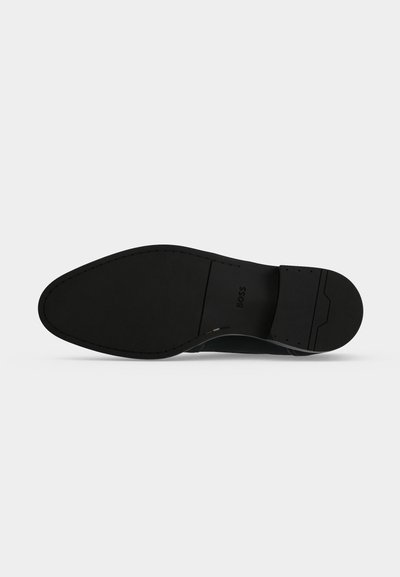 Semelle de chaussure habillée en cuir noir avec détail de couture et nom de marque embossé « "BOSS" » près de la zone du talon.