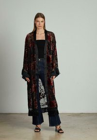 Kimono transparent negru cu un model floral roșu, cu detalii din franjuri la mâneci și tiv, purtat cu un top negru și blugi evazați albaștri.