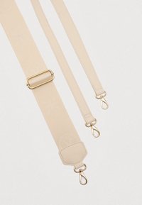 Bež nastavljiv pas za torbo z rožnatimi vzorci in zlatimi kovinskimi vrtljivimi zaponkami na belem ozadju.