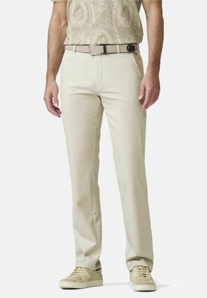 Man in beige recht gesneden broek, beige geweven riem, beige poloshirt met patroon en beige sneakers, staand tegen een witte achtergrond.