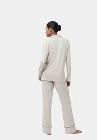 Ensemble de pyjama beige clair avec manches longues et pantalon. Comprend une chemise à col et un contraste au niveau des poignets et des ourlets du pantalon. Tissu doux et texturé.