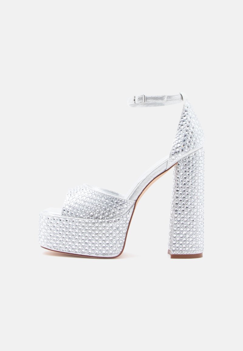Stříbrné sandály na vysokém podpatku s platformou, zdobené nýty, s širokým blokovým podpatkem, poutkem kolem kotníku a hladkým, lesklým povrchem.