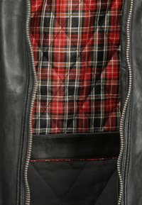 Svart läderjacka med fodrad röd och svart rutig insida, med ett diagonalt rutmönster och en silverfärgad dragkedja.