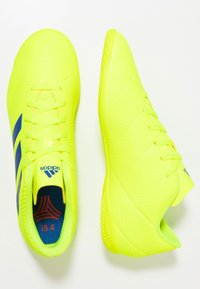 Scarpe da calcio gialle brillanti con dettagli blu, tomaia in materiale sintetico testurizzato, chiusura con lacci e soletta imbottita etichettata "18.4".