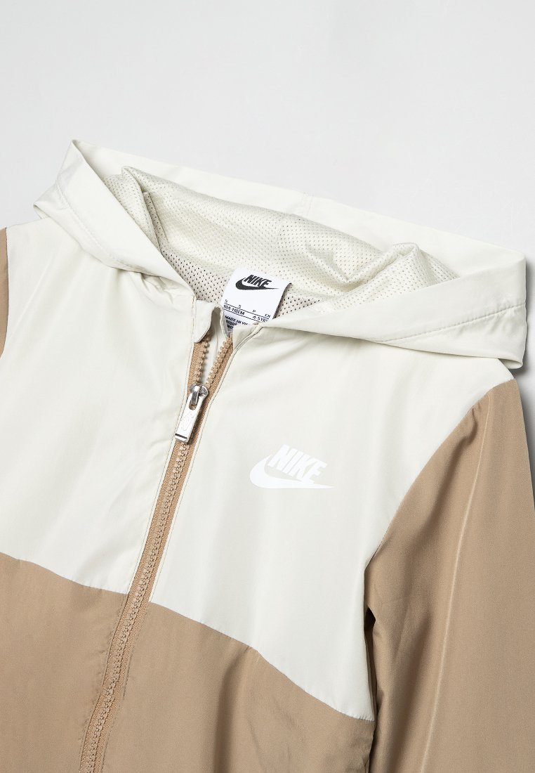 Veste zippée beige et blanche de Nike avec capuche, doublure en mesh et logo de la marque visible sur la poitrine.