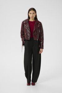 Burgundy faux leather cropped biker jacket with reptile pattern, silver hardware, paired with a red top and loose-fitting black trousers.