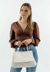 Witte handtas met een textuur onderkant en een gladde bovenkant, gecombineerd met een bruin langemouwen top en blauwe spijkerbroek. Eenvoudige hardware en strakke lijnen.