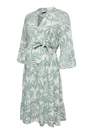White knee-length maternity dress with green leafy pattern, three-quarter bell sleeves, V-neck, and front tie at the waist.