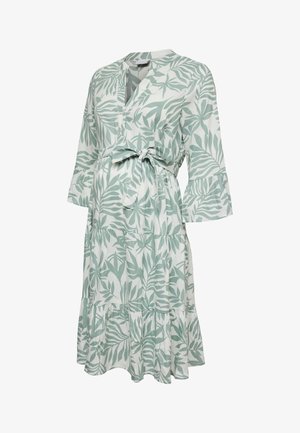 White knee-length maternity dress with green leafy pattern, three-quarter bell sleeves, V-neck, and front tie at the waist.