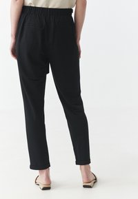Pantaloni neri con una vestibilità comoda, dotati di una cintura elastica, tasche laterali e orli arrotolati. Il tessuto sembra morbido, leggero e con una texture.