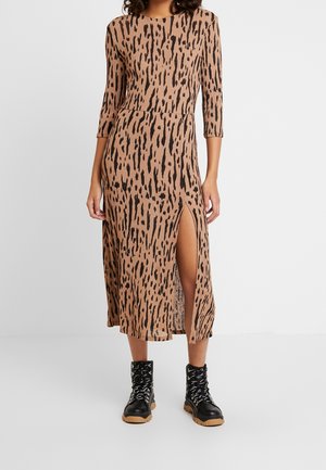 Mujer con un vestido midi marrón con manchas abstractas negras, mangas tres cuartos, abertura lateral y botas negras con cordones y suelas color beige.