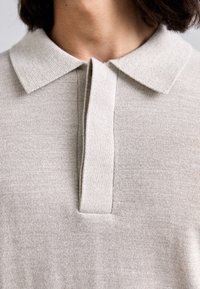 Polo en maille beige avec un col côtelé, une patte de boutonnage à moitié et une texture lisse, conçu dans un style simple et classique.