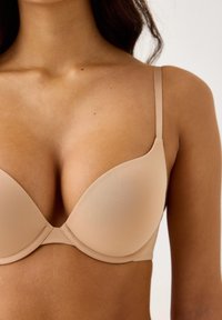 Sutiã acolchoado bege com aro, alças ajustáveis, textura suave e brilho subtil. Projetado para modelar e apoiar.