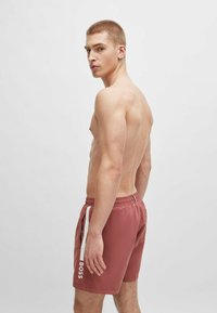 Røde badebukser med hvide sideaccenter og et logo. Fremstillet af letvægtsmateriale, med elastisk talje og en afslappet pasform.