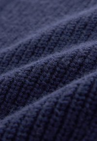 Gros plan d’un tissu tricoté bleu foncé avec une texture côtelée et des fibres douces et duveteuses visibles à la surface.