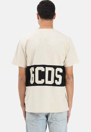 T-shirt beige in cotone con maniche corte, caratterizzata da una fascia orizzontale nera con lettere bianche a blocchi "6CDS" sul retro. Scollo rotondo, vestibilità rilassata.