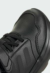 Schwarzer Sneaker aus strukturiertem Leder mit hohem Design, ausgestattet mit flachen Schnürsenkeln und einer glatten Gummisohle. Abgerundet mit drei seitlichen Streifen.