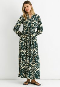 Long, green dress with cream floral patterns, button-down front, elastic waist, and tiered skirt. Paired with black flip-flops.