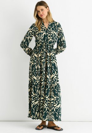 Long, green dress with cream floral patterns, button-down front, elastic waist, and tiered skirt. Paired with black flip-flops.
