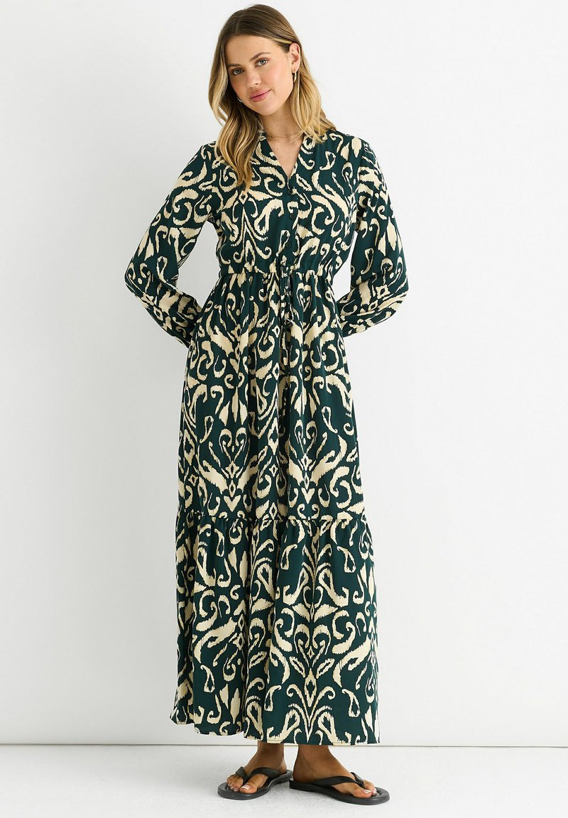 Long, green dress with cream floral patterns, button-down front, elastic waist, and tiered skirt. Paired with black flip-flops.