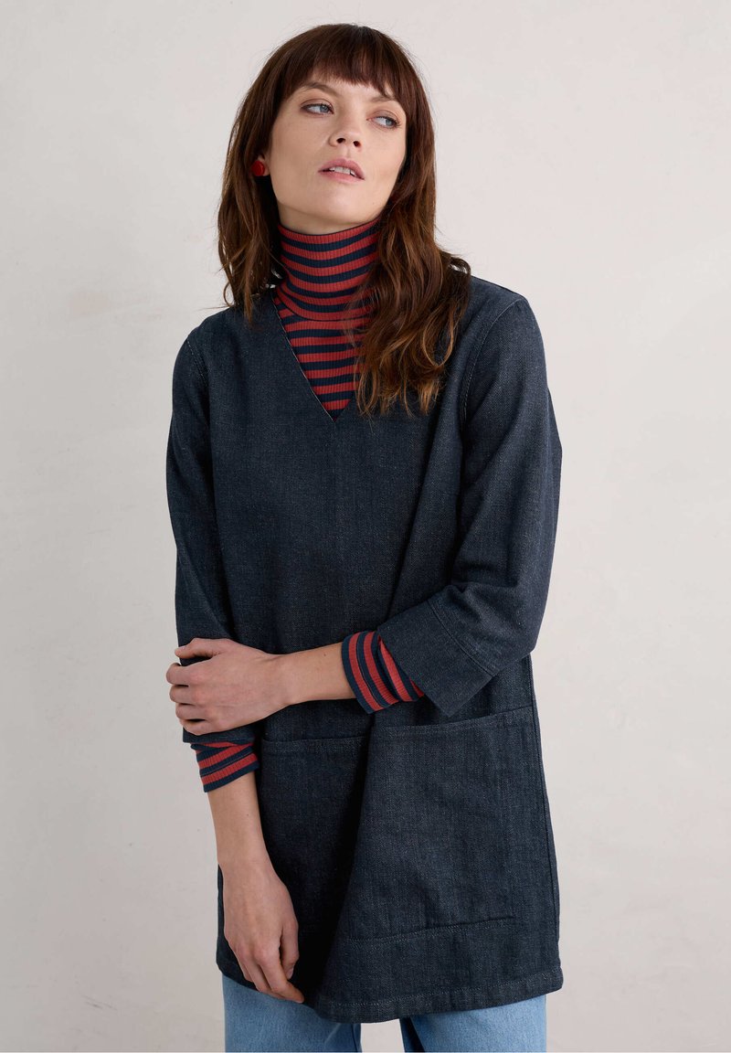 Tunique en denim bleu foncé avec un col en V et des manches trois quarts, dotée de poches à l'avant et d'un turtleneck rayé rouge et marine superposé en dessous.