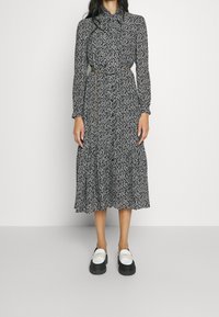 Svart- och vittryckt klänning med långa ärmar, kragdetalj, elastisk midja och flerlagad kjol, kombinerad med klumpiga svart- och vitfärgade skor.