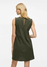 Vestido corto verde oliva con bordes de las mangas en forma de concha, detalle de abertura en la espalda y tejido texturizado, que cae por encima de la rodilla.