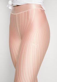 Leggings rosa chiaro con un motivo a strisce ondulate, vita elasticizzata e un piccolo logo bianco. Materiale liscio e elasticizzato con una finitura lucida.