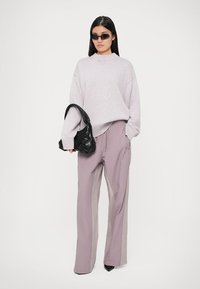 Suéter de malha cinza claro, de corte largo. Calças lilases de cintura alta com corte reto. Modelo segura uma bolsa preta texturizada, usando óculos de sol pretos.