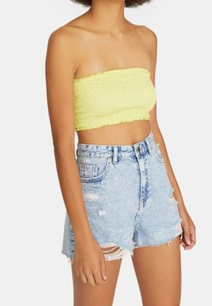 Person, der bærer en gul stropløs top og højtaljede, lyseblå, slidte denimshorts med frynset kant.