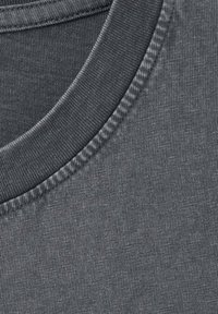 Gros plan sur un tissu de t-shirt gris, présentant une texture lisse, un col rond côtelé et des coutures régulières le long des bords.