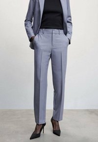 Light gray tailored trousers with a slim fit, featuring front pleats and side pockets, paired with black high-heeled shoes.