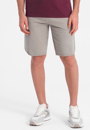 Shorts gris clair en matériau doux, avec une texture lisse, coupe droite et coutures contrastées ; accompagnés de baskets blanches et grises.