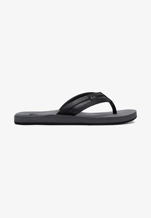 Musta flip-flop, jossa on pehmeä kumipohja, kaksi teksturoitua remmiä, selkeä logo ja tasainen, sileä pohja.
