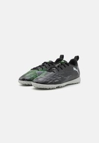 Schwarze Sportschuhe mit grünen Akzenten, versehen mit einem strukturierten Obermaterial mit einem Mustermuster und einer hellgrauen Gummisohle für besseren Halt.