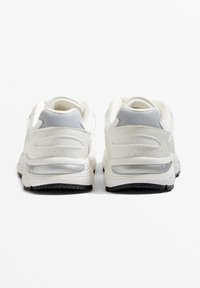 Białe sneakersy o gładkiej fakturze, z panelami z siateczki i jasnoszarymi akcentami na pięcie. Posiadają widoczną jednostkę poduszkową i czarną podeszwę.